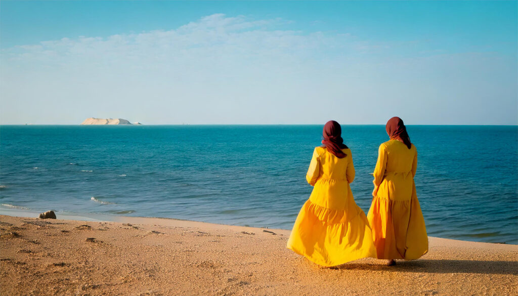 Jadayel ontact us - a landscape of 2 qatari women wearing yellow clark on the beach